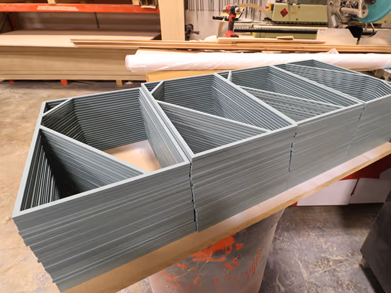 Stacks of custom painted blue-grey acrylic frames for room ID signs in production at Exhibit Studio's fabrication shop in Calgary, part of the nearly 400-sign wayfinding system produced for Ronald McDonald House Alberta Calgary House in collaboration with