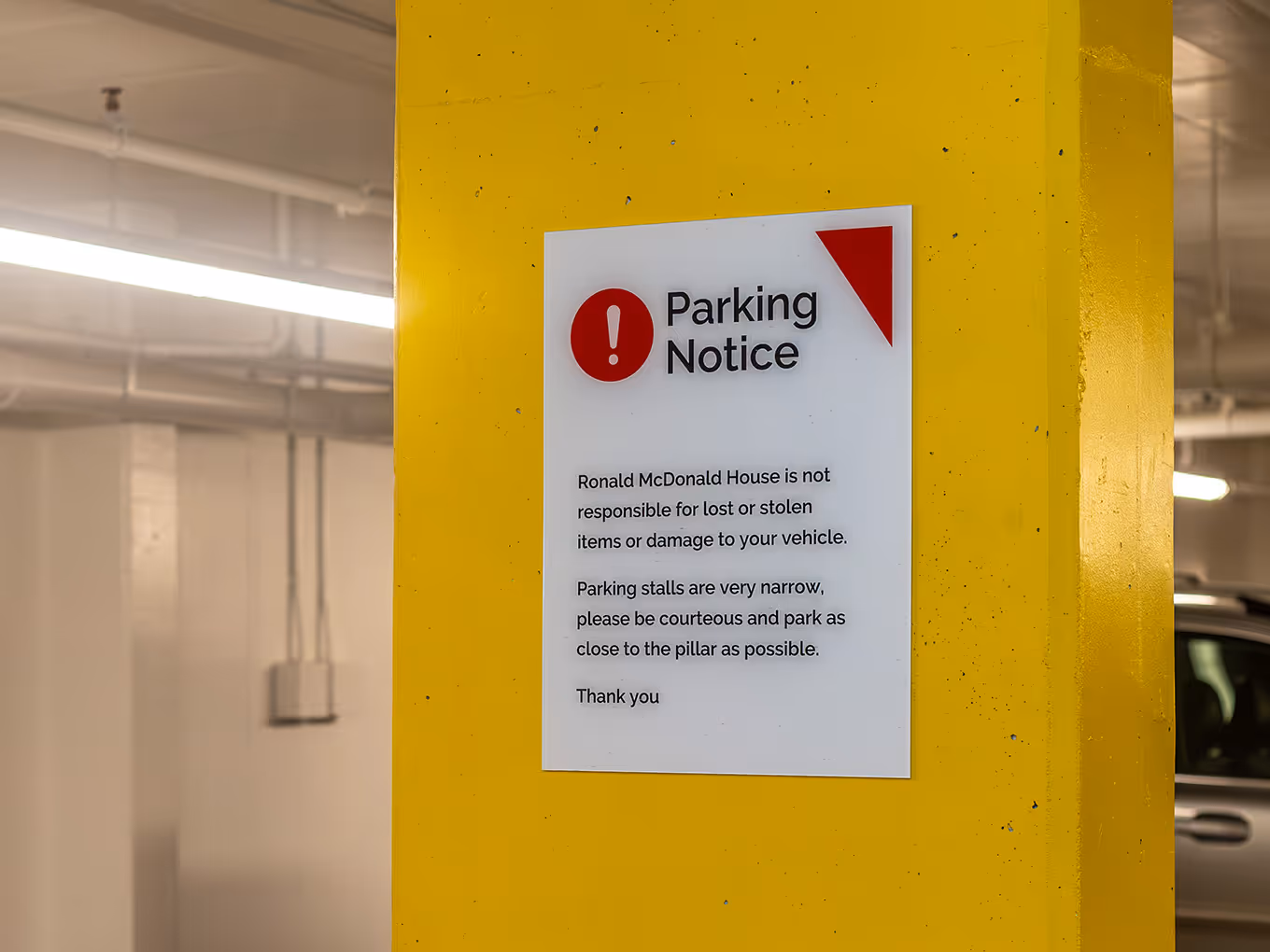 Custom parking notice sign mounted on a yellow parkade pillar at Ronald McDonald House Alberta Calgary House, produced by Exhibit Studio.