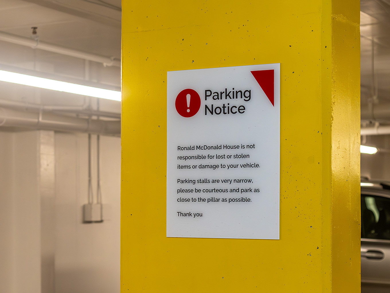 Custom parking notice sign mounted on a yellow parkade pillar at Ronald McDonald House Alberta Calgary House, produced by Exhibit Studio.