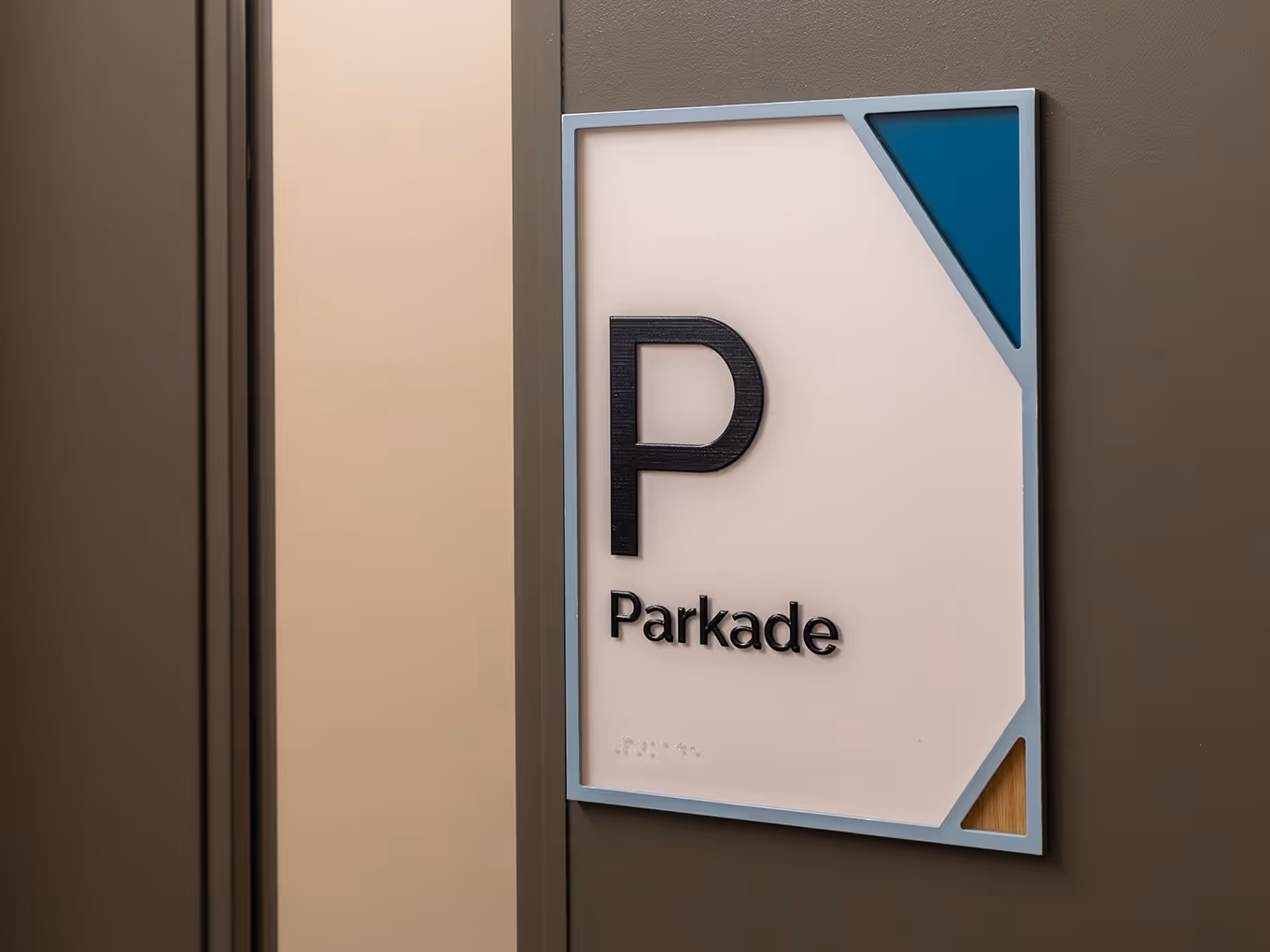 Custom accessible parkade room ID sign with dimensional "P" icon, braille panel, teal corner graphic, and painted acrylic frame at RMHC Calgary House.