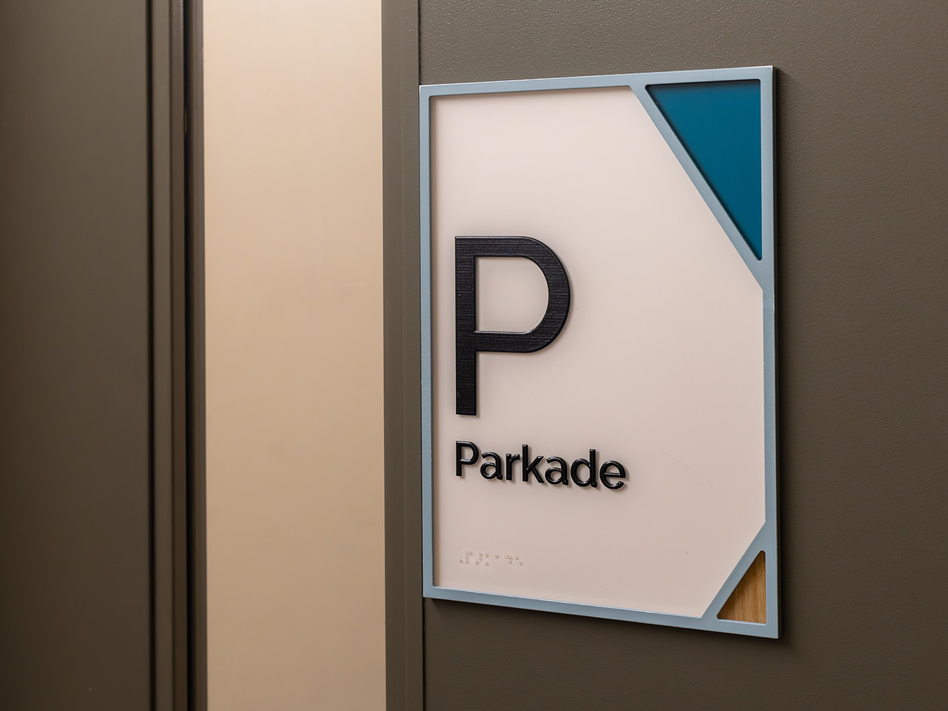 Custom accessible parkade room ID sign with dimensional "P" icon, braille panel, teal corner graphic, and painted acrylic frame at RMHC Calgary House.