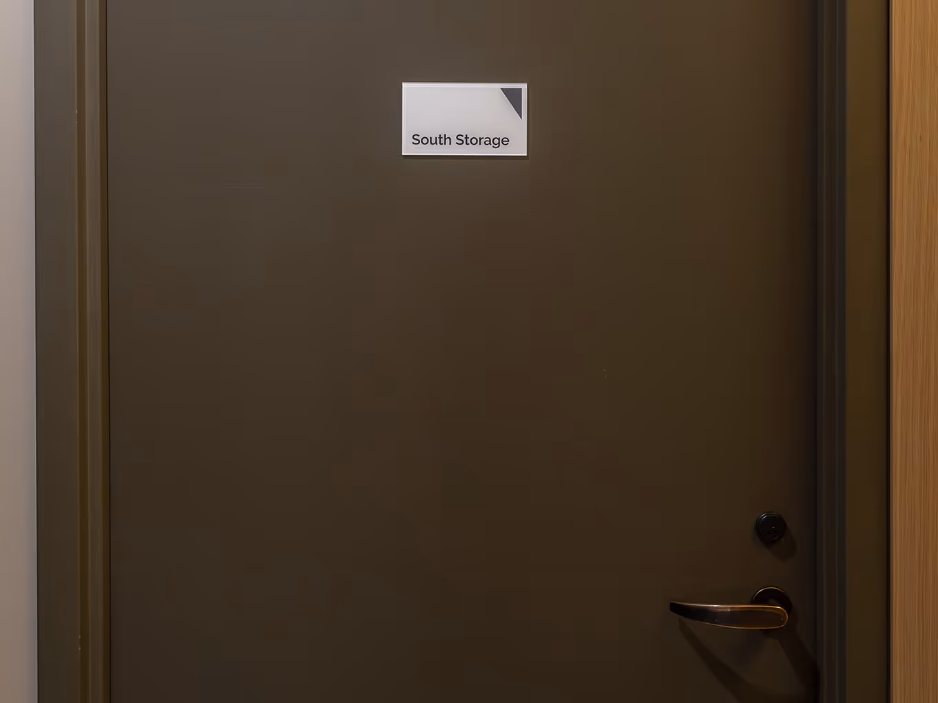 Small custom wayfinding sign reading "South Storage" mounted on a door at Ronald McDonald House Alberta Calgary House, fabricated by Exhibit Studio.