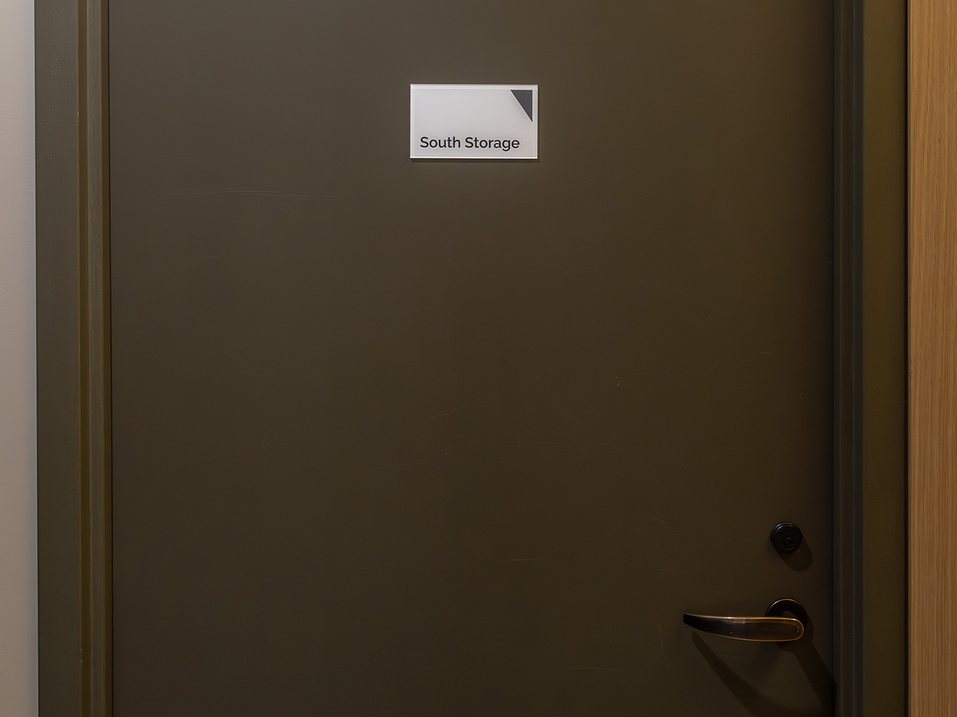 Small custom wayfinding sign reading "South Storage" mounted on a door at Ronald McDonald House Alberta Calgary House, fabricated by Exhibit Studio.