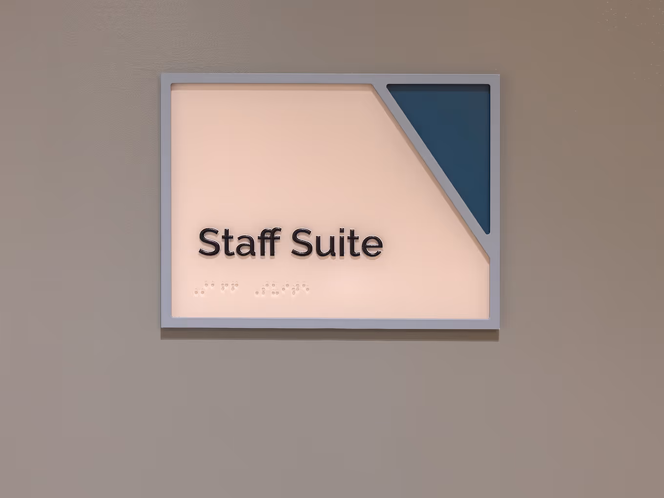 Accessible room ID sign for Staff Suite at RMHC Calgary House, featuring dimensional lettering, braille panel, painted acrylic frame, and teal corner graphic.