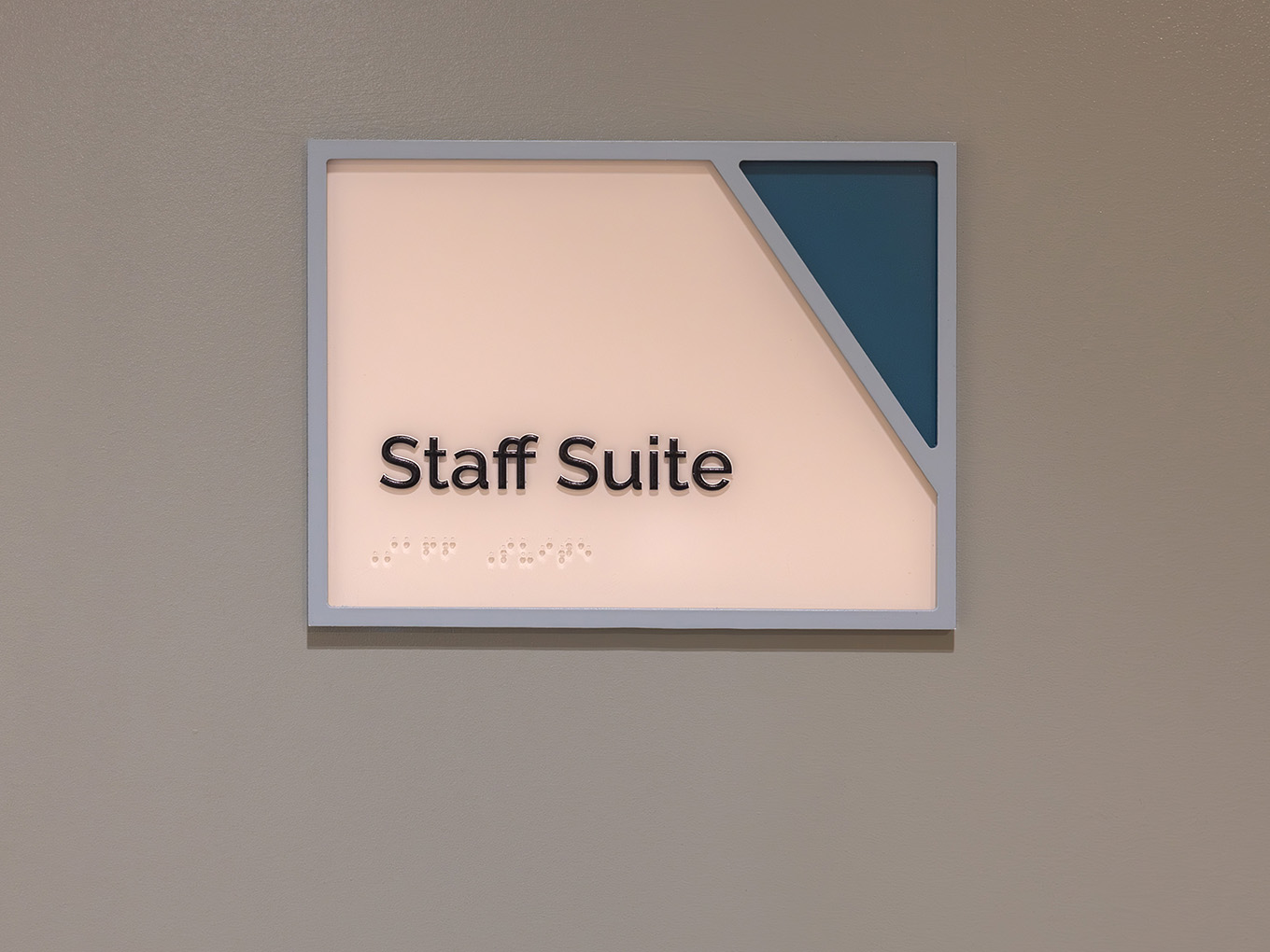 Accessible room ID sign for Staff Suite at RMHC Calgary House, featuring dimensional lettering, braille panel, painted acrylic frame, and teal corner graphic.