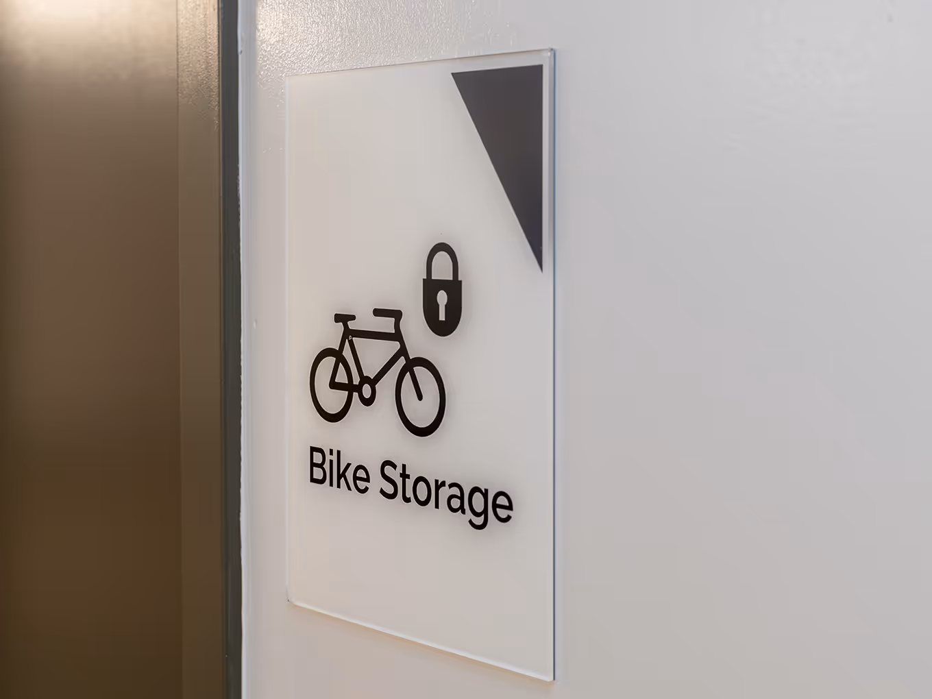 Custom wayfinding sign for Bike Storage at Ronald McDonald House Alberta Calgary House, featuring dimensional bicycle and lock icons on a clear acrylic panel.