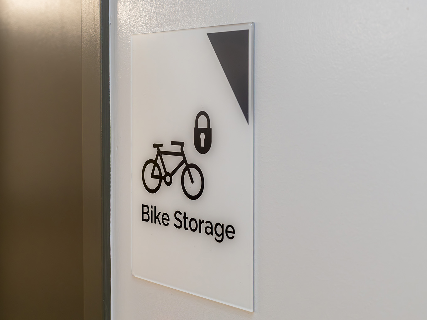 Custom wayfinding sign for Bike Storage at Ronald McDonald House Alberta Calgary House, featuring dimensional bicycle and lock icons on a clear acrylic panel.