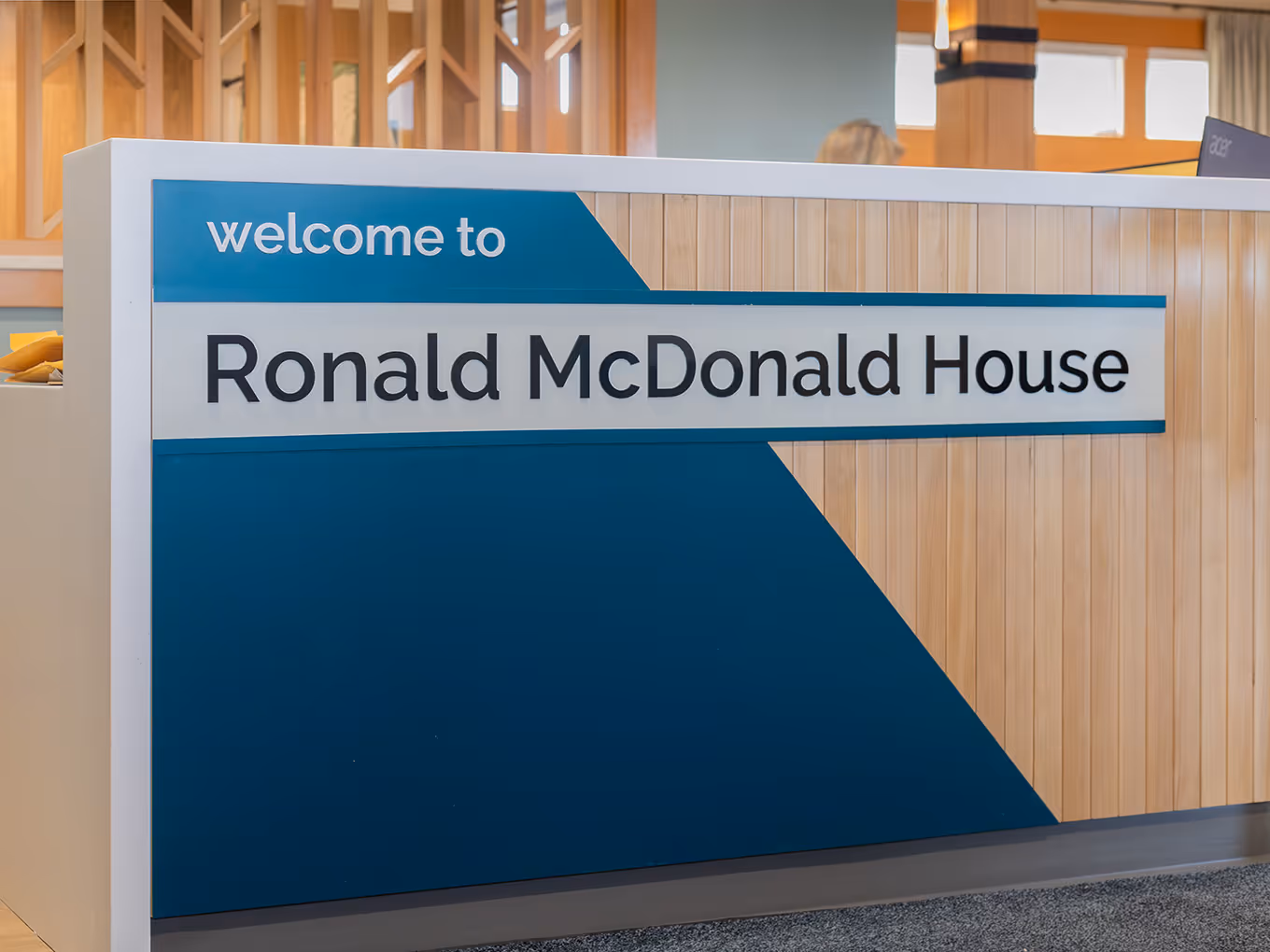 Branded reception desk signage reading "Welcome to Ronald McDonald House" with teal and white acrylic panels, fabricated and installed by Exhibit Studio Calgary.
