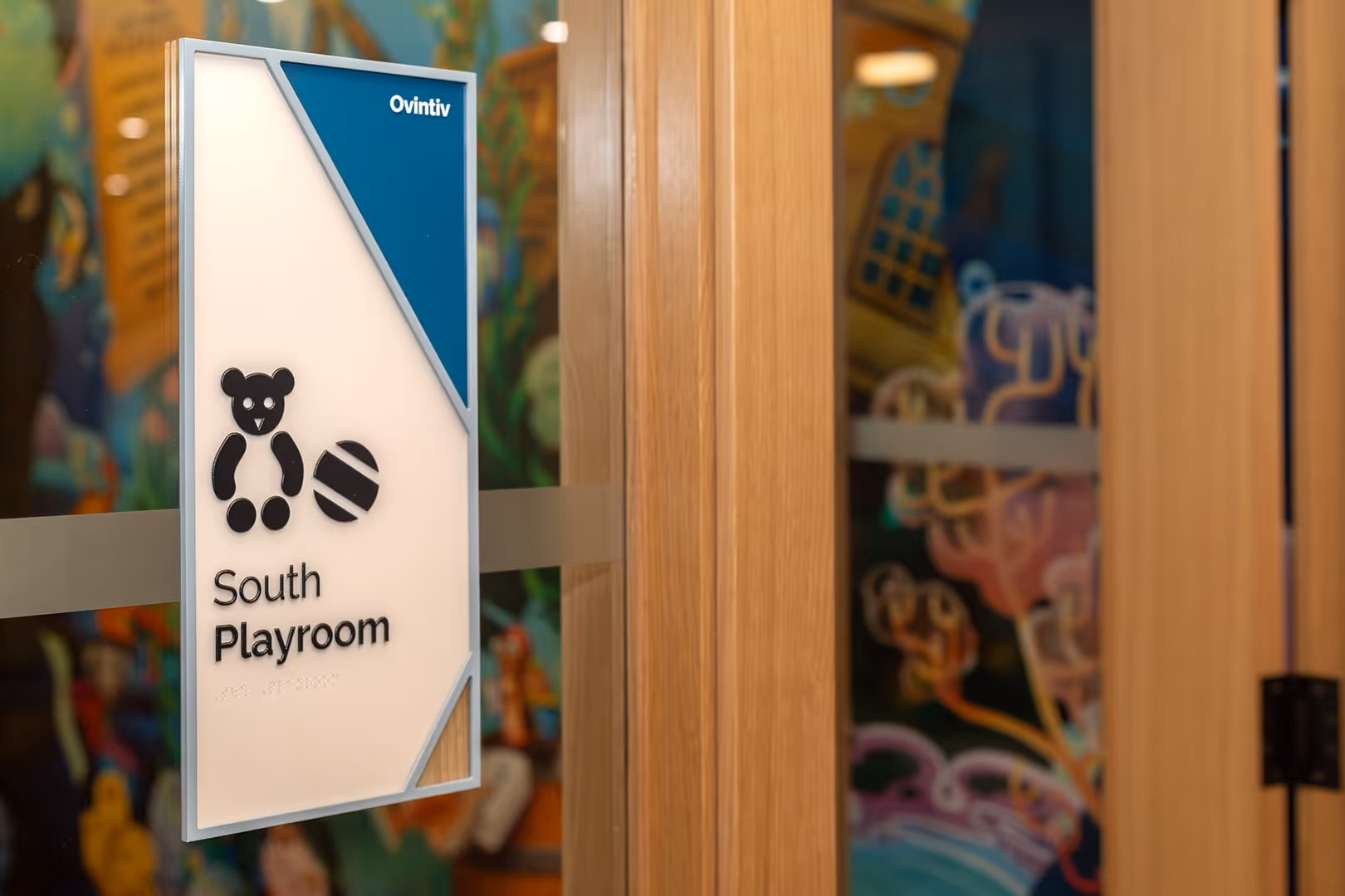 Window-mounted wayfinding sign for “South Playroom” featuring iconography and clear, child-friendly design.