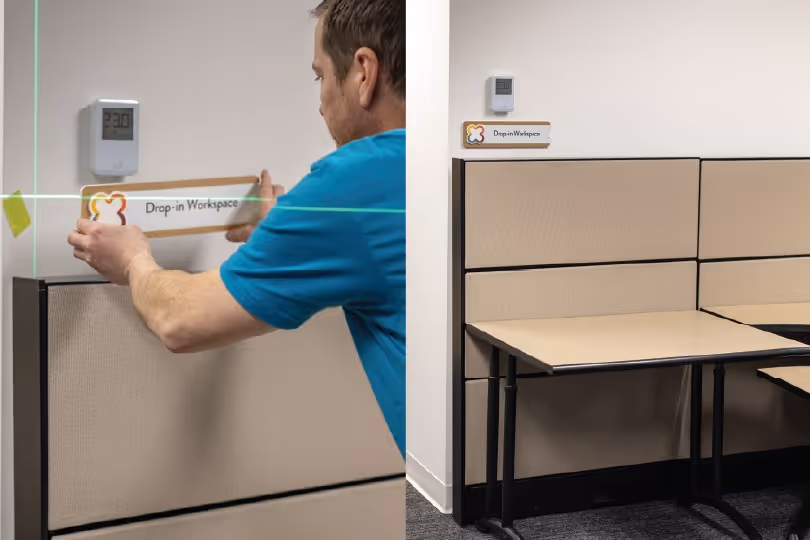two images, left showing a vertical wayfinding sign displaying an open work space and the right image showing the signage being installed.
