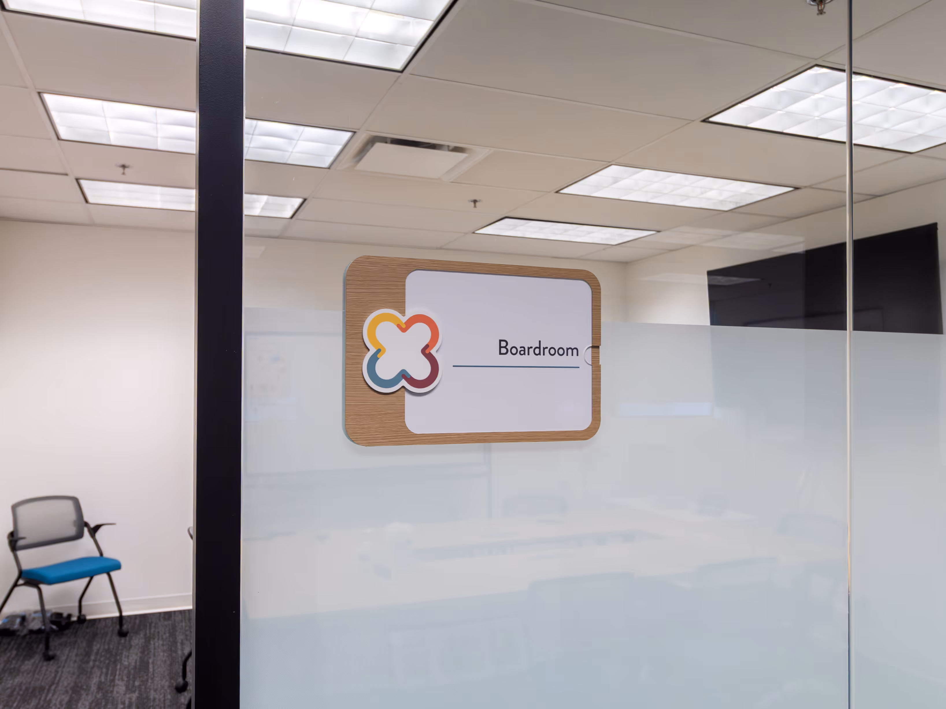 Boardroom plaque on a frosted glass wall, with the conference room interior and a chair visible beyond.