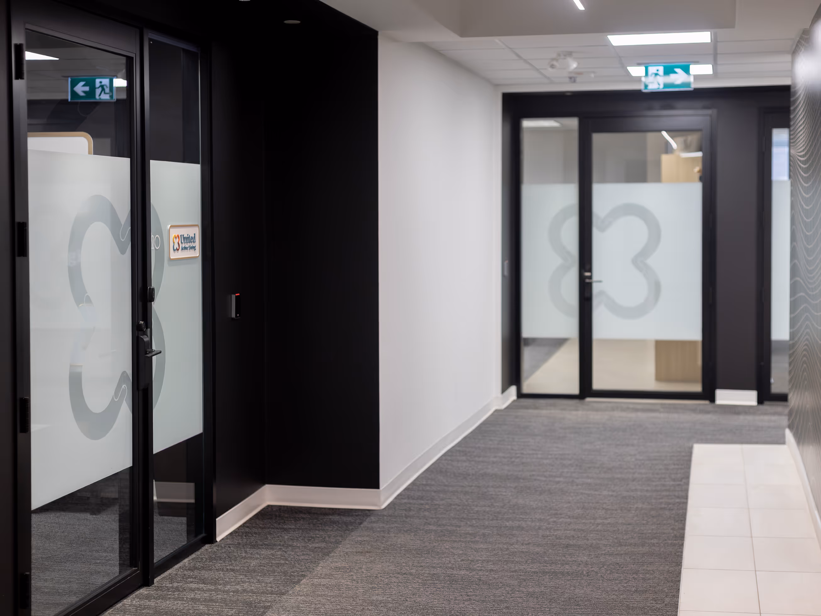 Calgary Beltline office corridor with frosted vinyl privacy film carrying the United Active Living butterfly logo across two sets of glass doors.