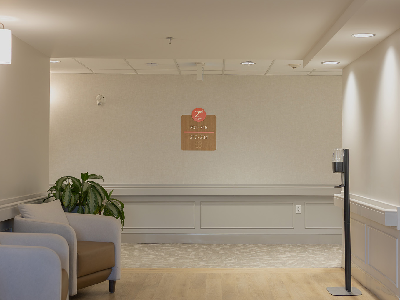 Wall-mounted second-floor wing identifier sign at United Active Living Garrison Green, displayed in a quiet lounge area with cream wainscoting, a soft armchair, and natural light.