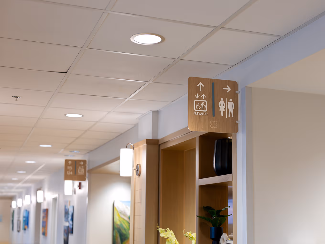 Long hallway view at United Active Living Garrison Green showing a coordinated wayfinding system, with multiple wall-mounted directional and elevator signs throughout the corridor.