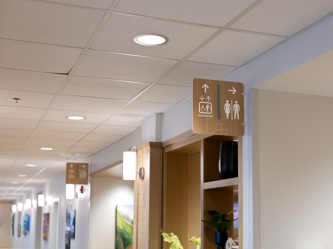Long hallway view at United Active Living Garrison Green showing a coordinated wayfinding system, with multiple wall-mounted directional and elevator signs throughout the corridor.