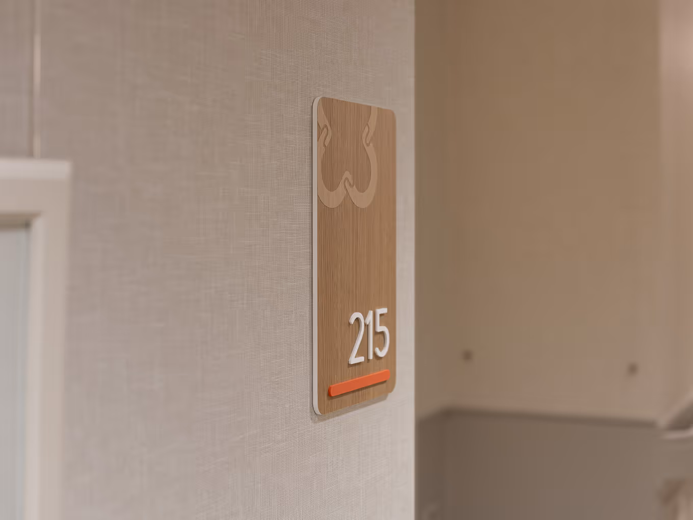 Vertical wood-look suite identification sign for unit 215 at United Active Living Garrison Green, with dimensional white numerals, a coral accent bar, and the United floral logo watermark at the top.