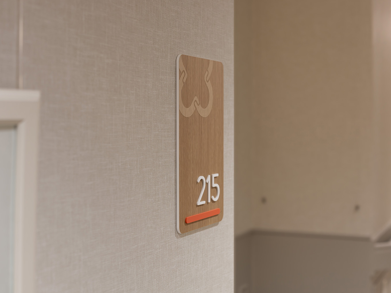 Vertical wood-look suite identification sign for unit 215 at United Active Living Garrison Green, with dimensional white numerals, a coral accent bar, and the United floral logo watermark at the top.