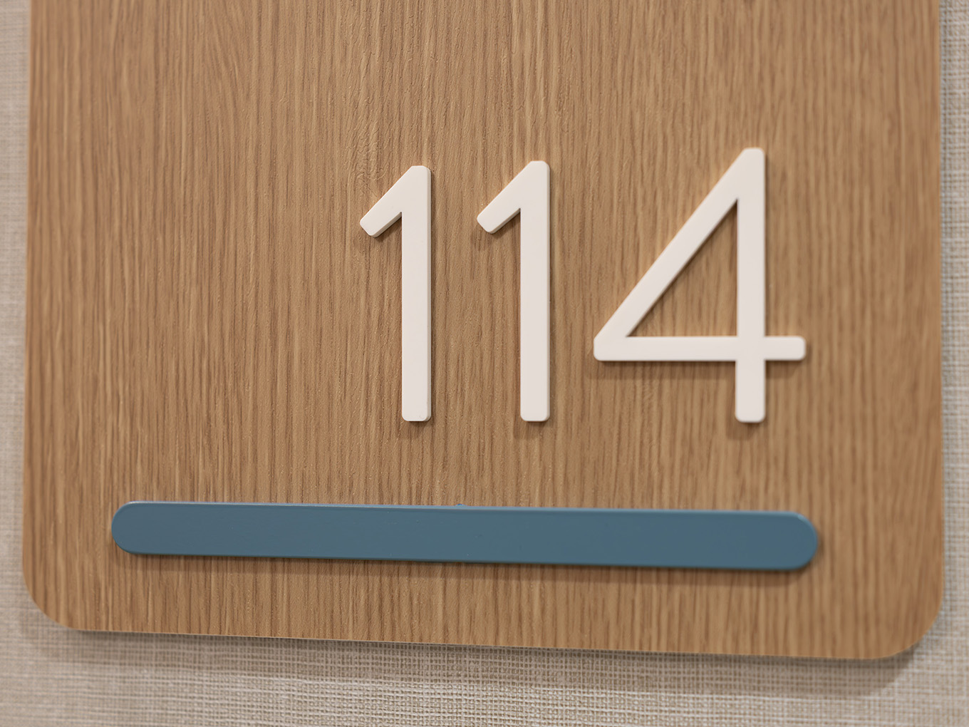 Macro detail of dimensional acrylic numbering on a wood-look suite sign at United Active Living Garrison Green, paired with a hand-trimmed blue accent bar.