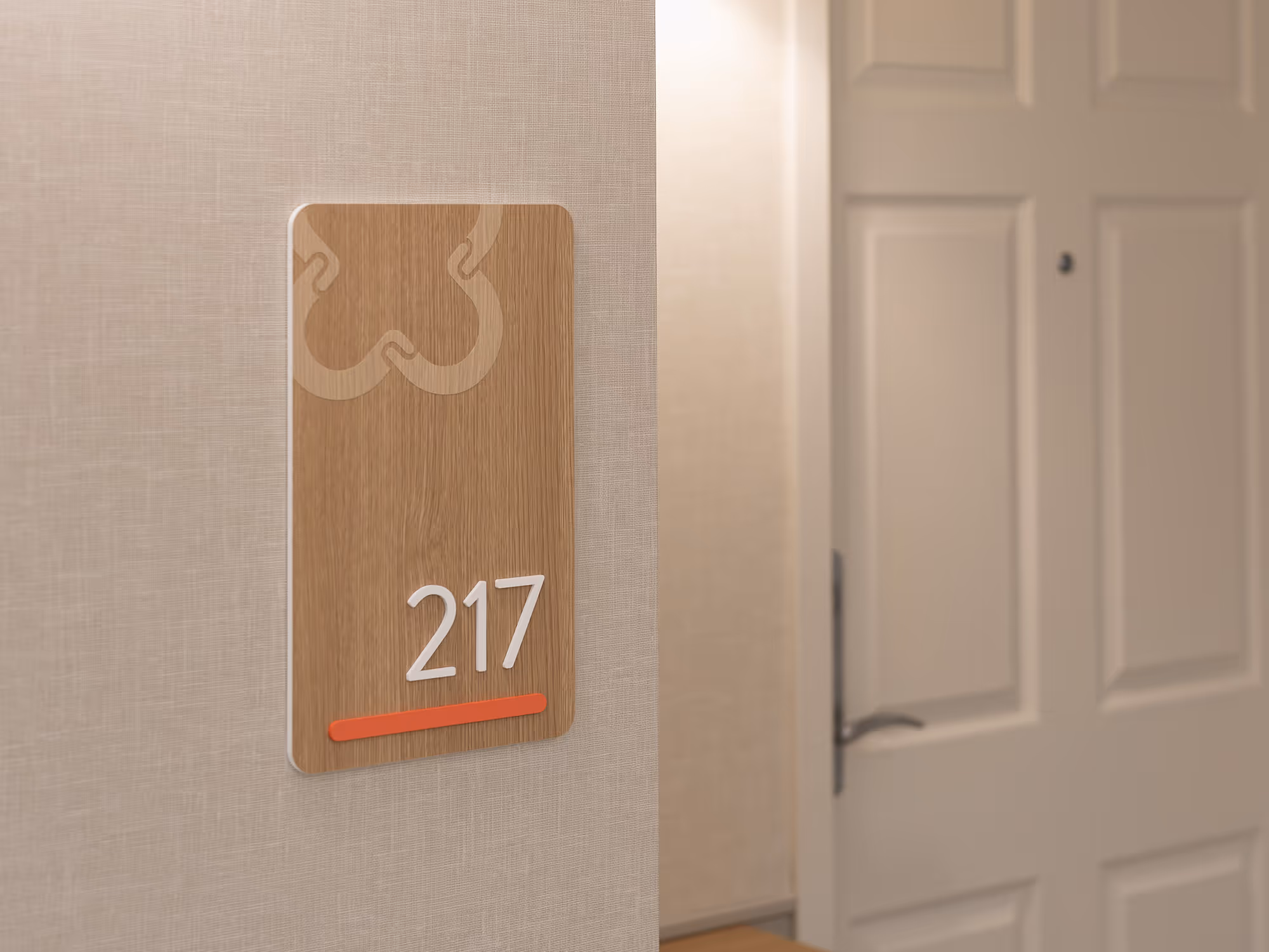 Detail view of the suite 217 wayfinding plaque at United Active Living Garrison Green, showing the wood-look finish, dimensional white numbers, and floor-coded coral accent bar.