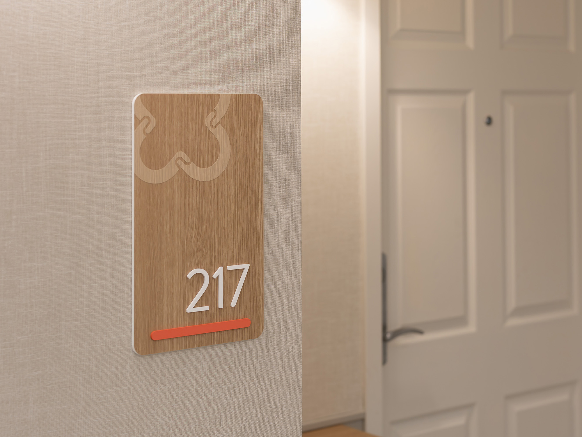 Detail view of the suite 217 wayfinding plaque at United Active Living Garrison Green, showing the wood-look finish, dimensional white numbers, and floor-coded coral accent bar.