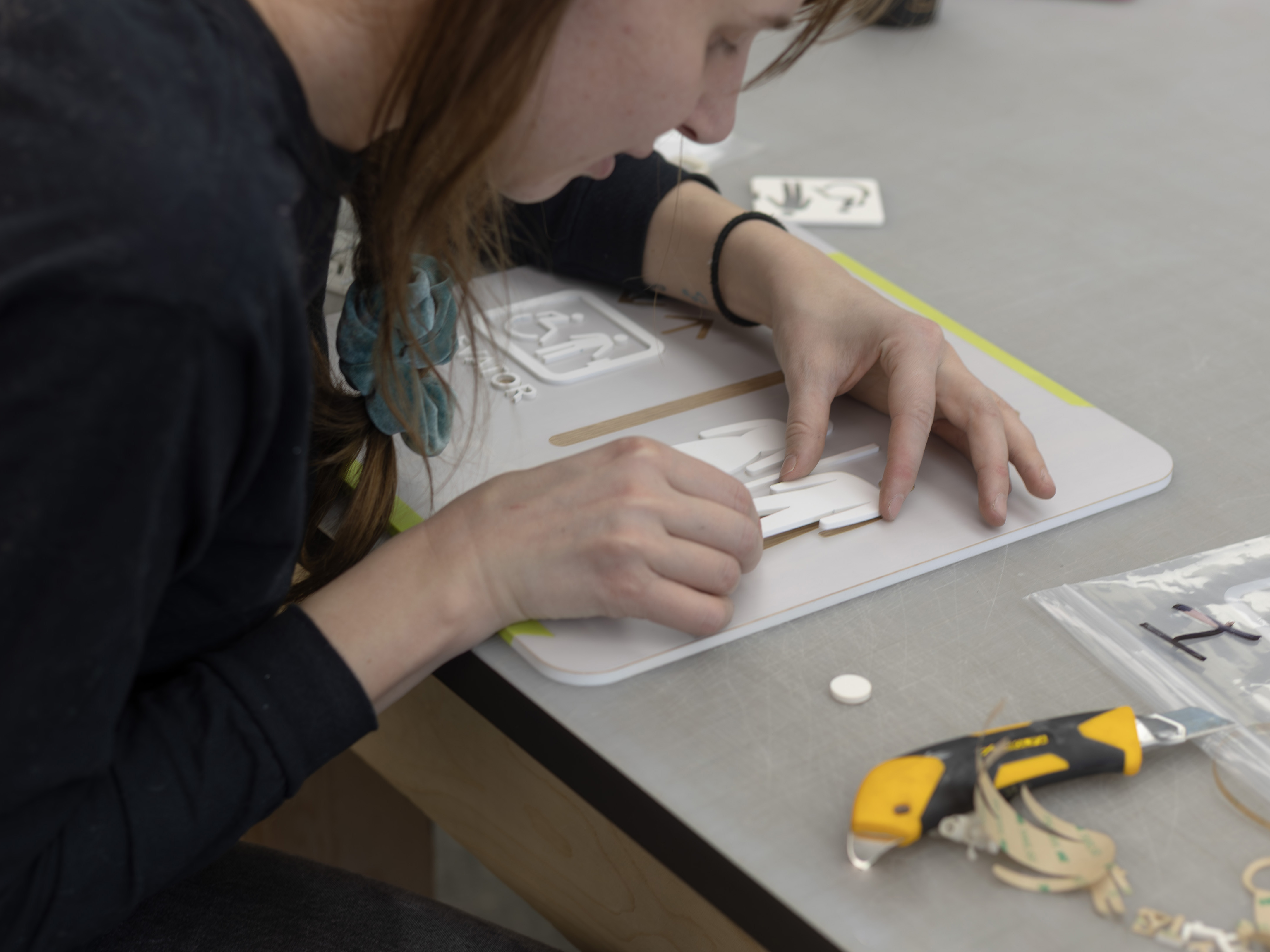 Behind the scenes at Exhibit Studio: a fabricator hand-applies dimensional acrylic lettering to a wayfinding panel as part of the United Active Living Garrison Green sign production.