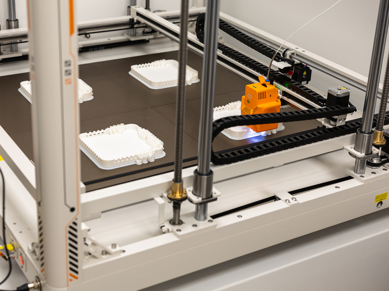 Elegoo OrangeStorm Giga print head actively printing four parts simultaneously on the large-format build plate at Exhibit Studio