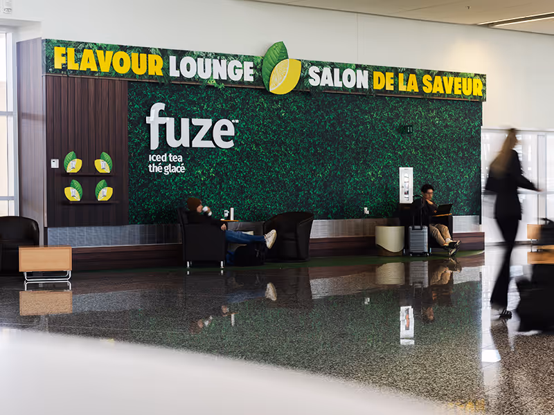 Airport travellers using Fuze Iced Tea Flavour Lounge seating area with green living wall backdrop at YYC Calgary Airport