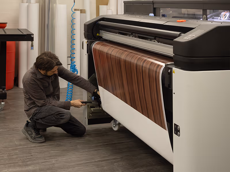 Print technician operating large-format printer producing wood-grain wrap for Fuze Iced Tea airport brand activation build
