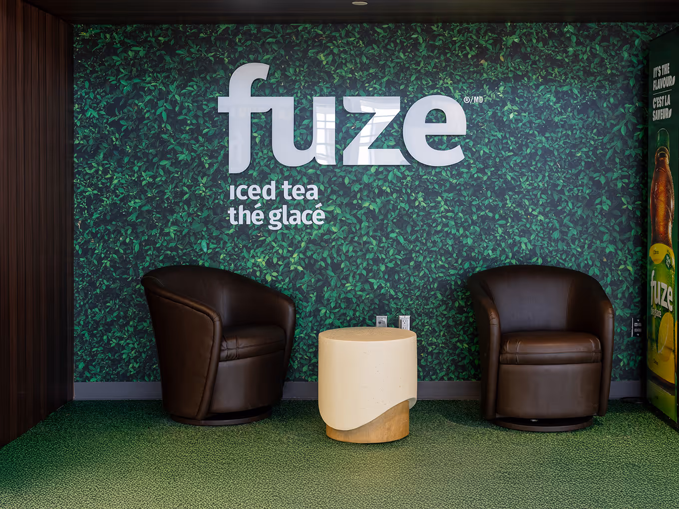 Fuze Iced Tea branded interior lounge area with green leaf wall mural and leather seating at YYC Calgary Airport