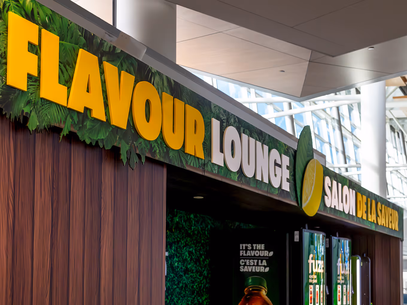 Custom Flavour Lounge dimensional signage with tropical foliage graphics above Fuze branded kiosk at Calgary Airport