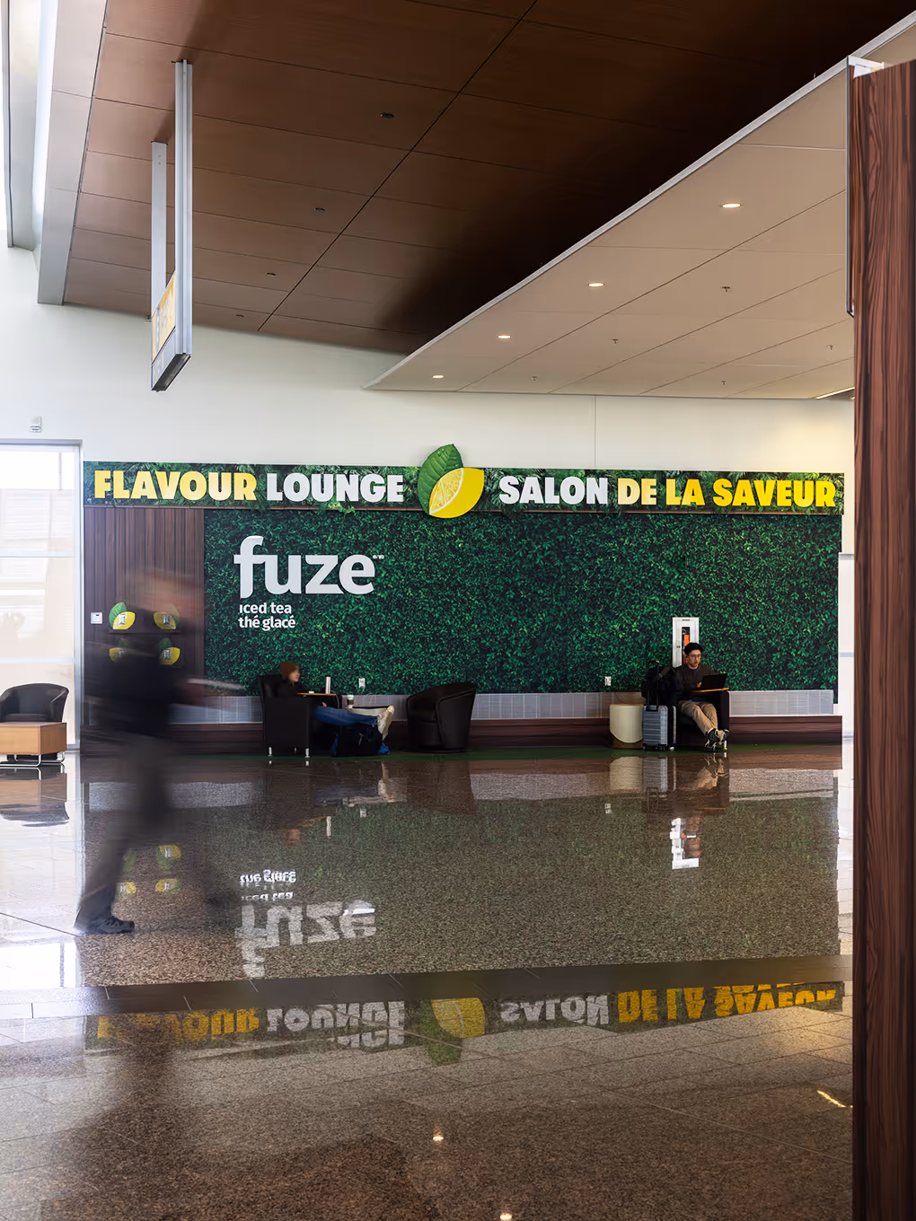 Wide view of Fuze Iced Tea Flavour Lounge airport brand activation with reflective floor and travellers at YYC