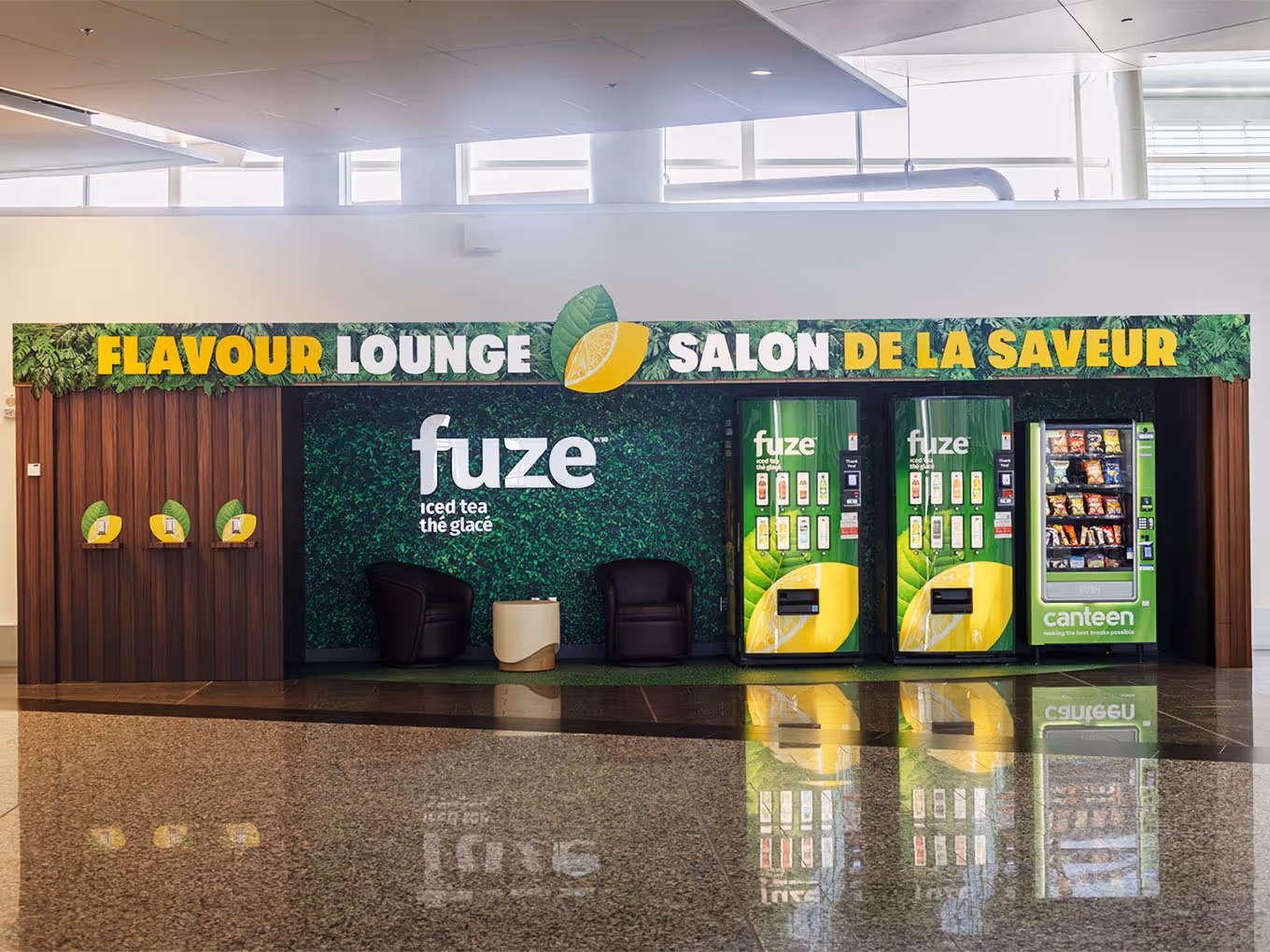 Full frontal view of Fuze Iced Tea Flavour Lounge brand activation with seating, vending, and bilingual signage at Calgary Airport