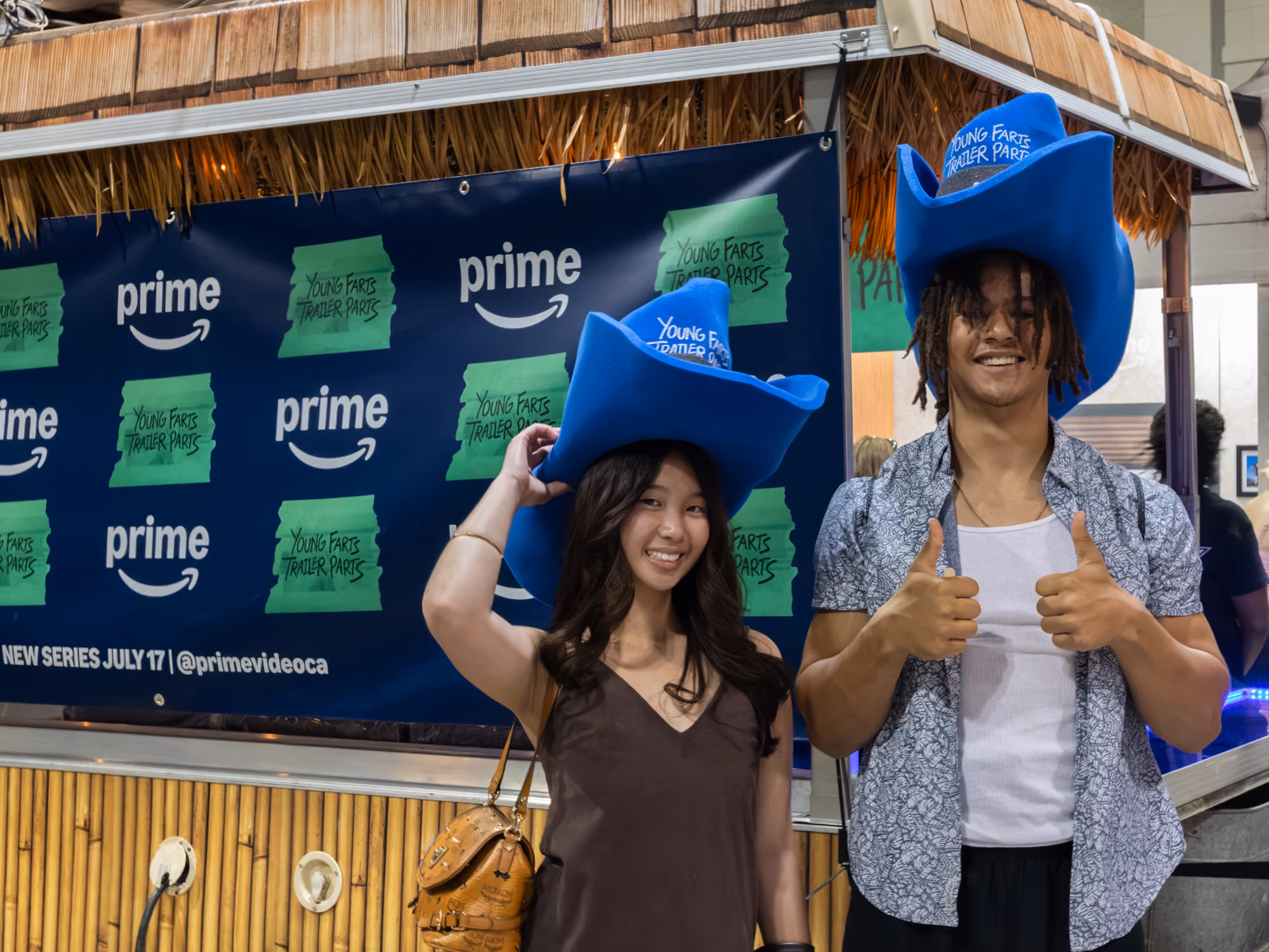Guests wear oversized blue cowboy hats in front of the Young Farts Trailer Parts branded backdrop at the activation.