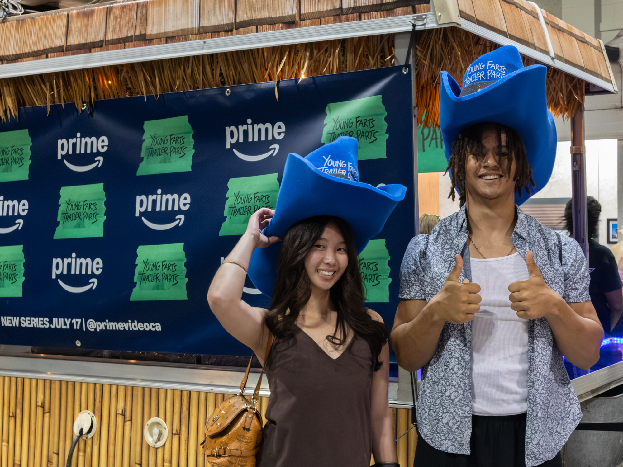 Guests wear oversized blue cowboy hats in front of the Young Farts Trailer Parts branded backdrop at the activation.
