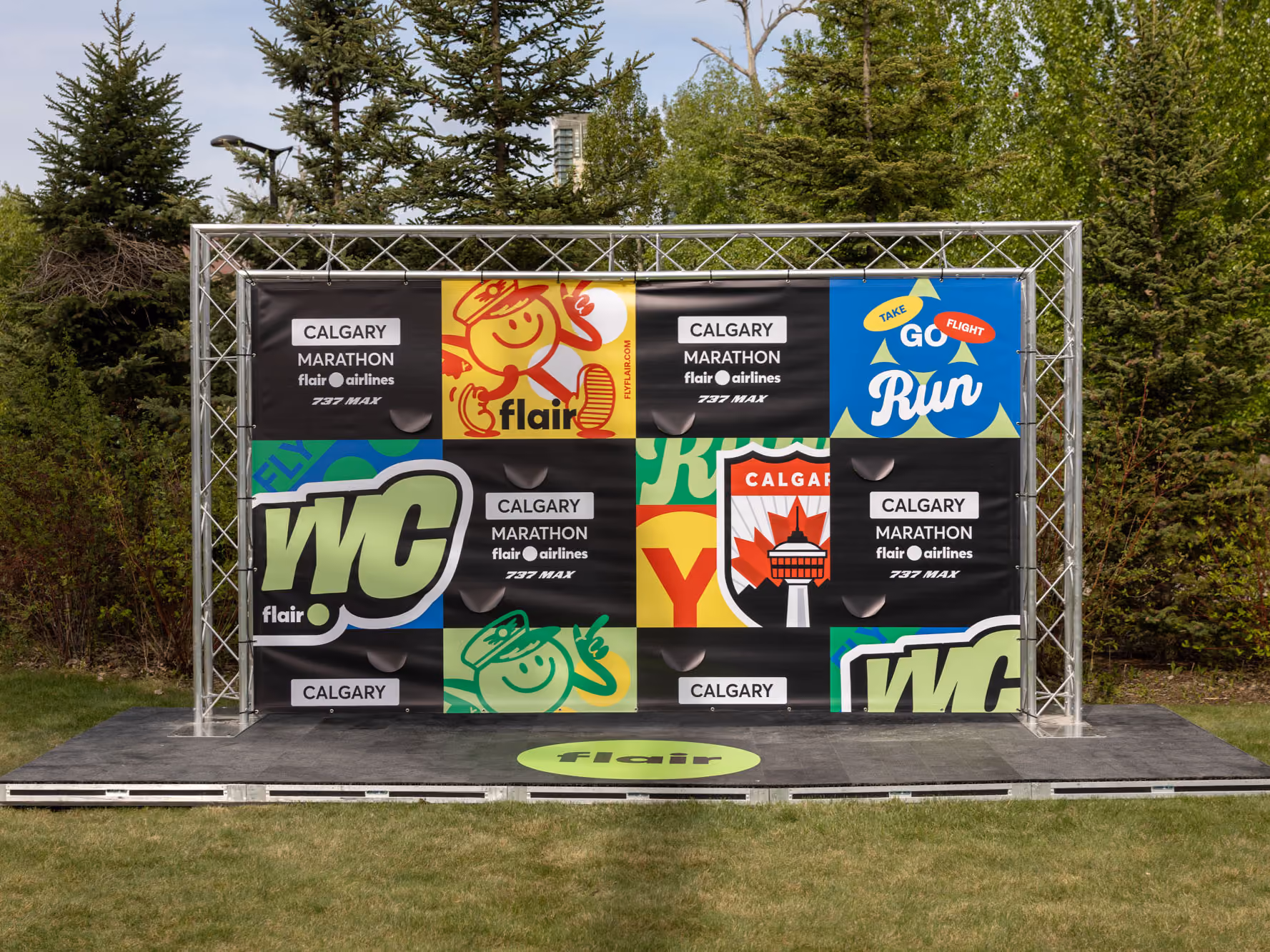 Front view of the finish-line photo backdrop with Flair, YYC and Calgary Marathon graphics and a green Flair circle on the stage floor.