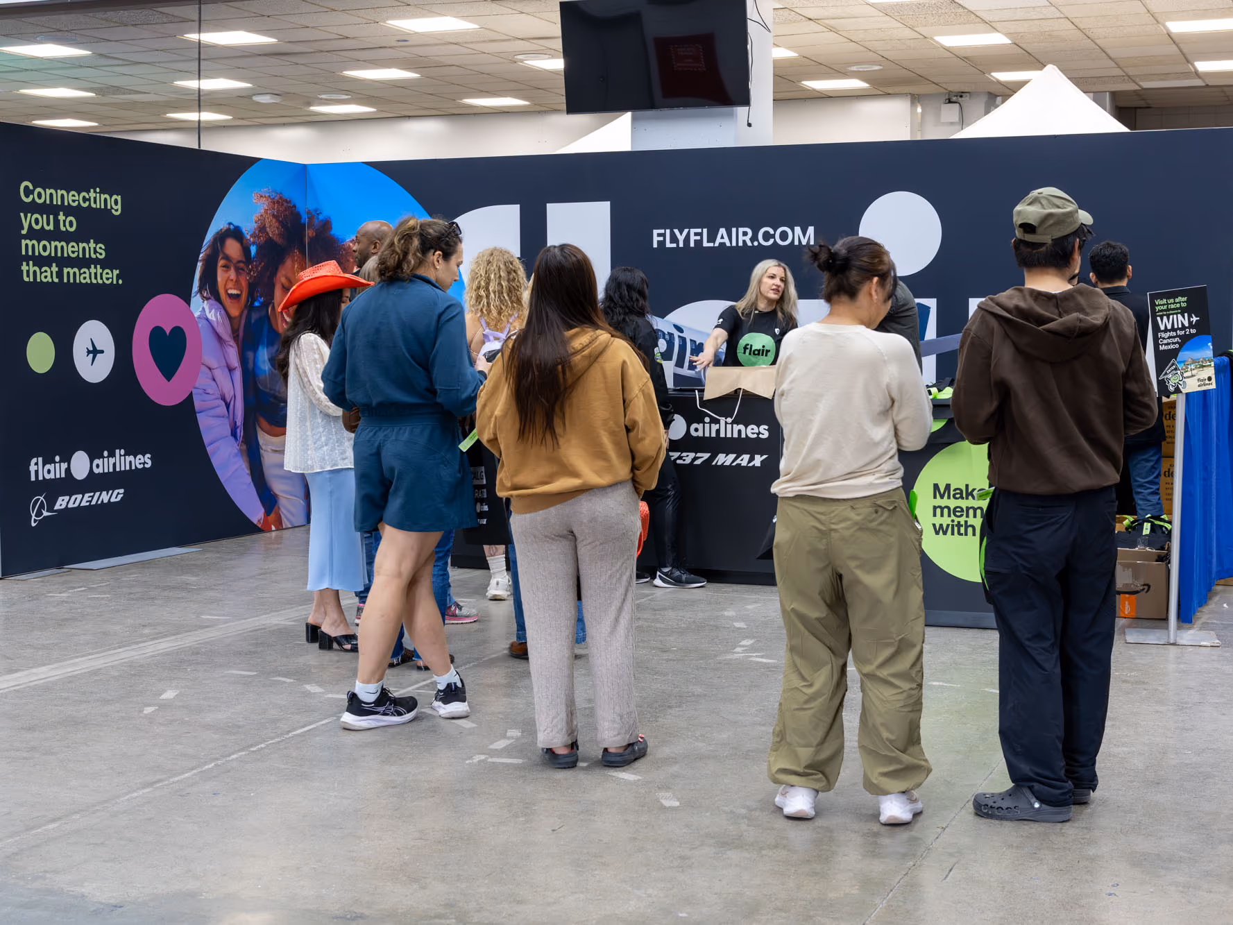 Visitors queue at the Flair booth while a staff member greets them at the counter, with a Flair logo and 737 MAX graphic on the wall.