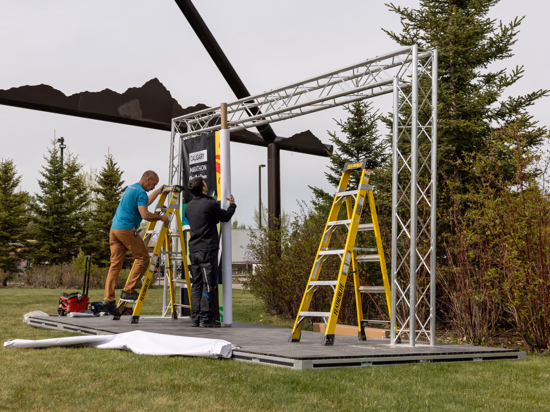 Two installers on ladders hang a printed vinyl banner on the aluminum truss on stage.