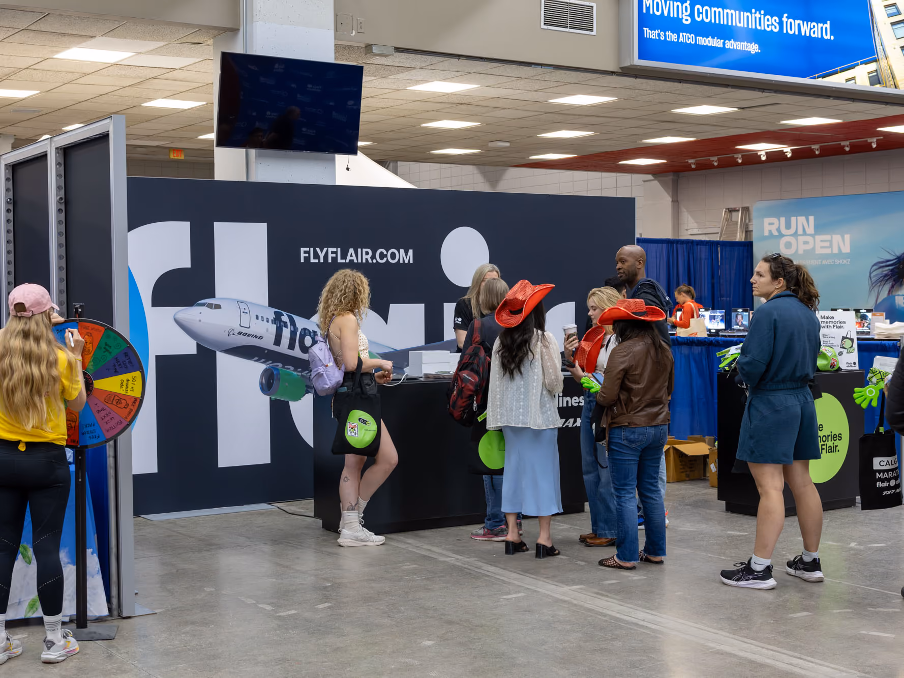 Crowd at the Flair booth with a prize wheel, red cowboy hats, and tote bags featuring a green Flair circle.