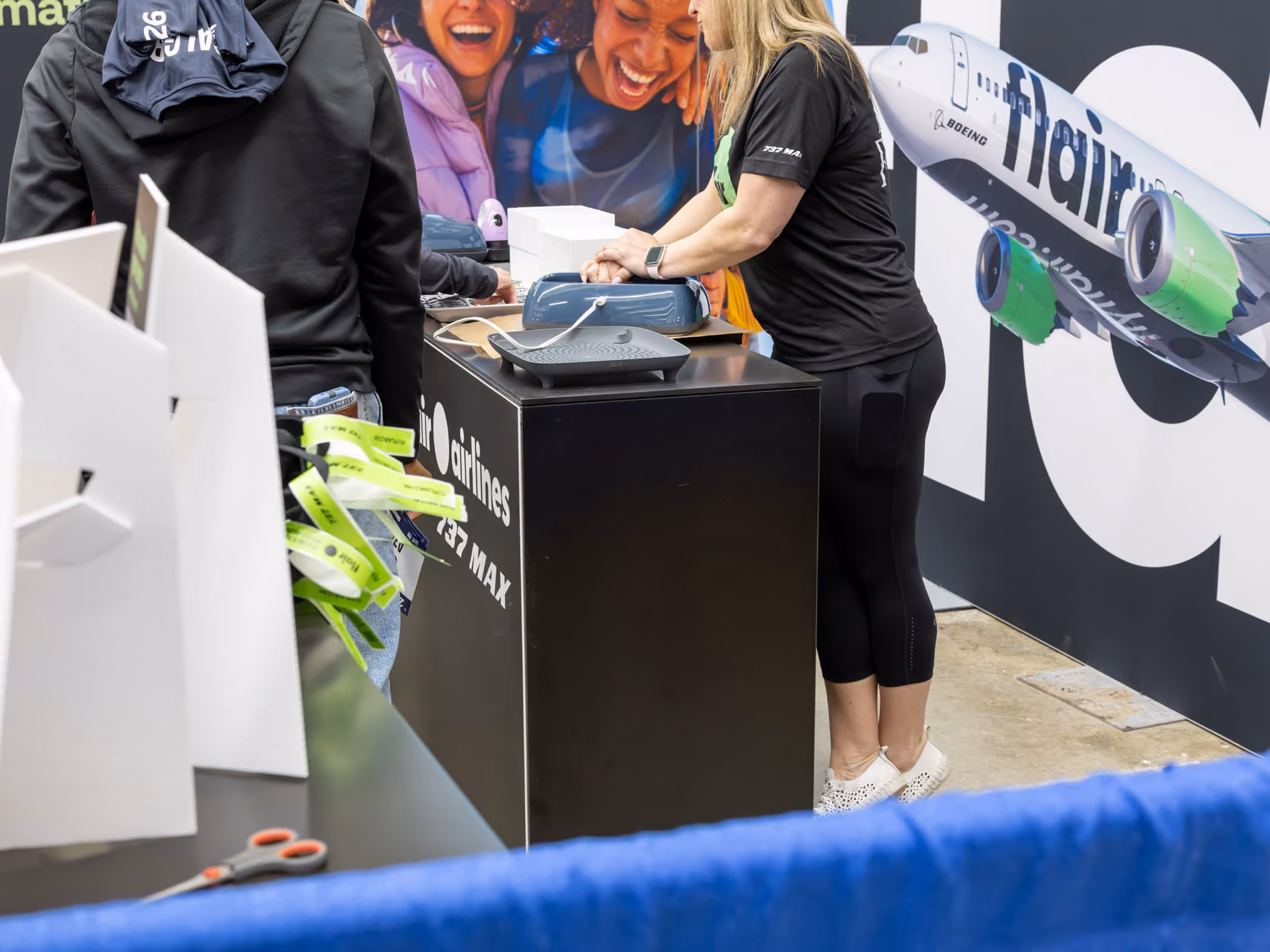 Flair booth counter with a green circle reading "Make memories with Flair" as visitors chat with staff in "Take Flight" run club shirts.