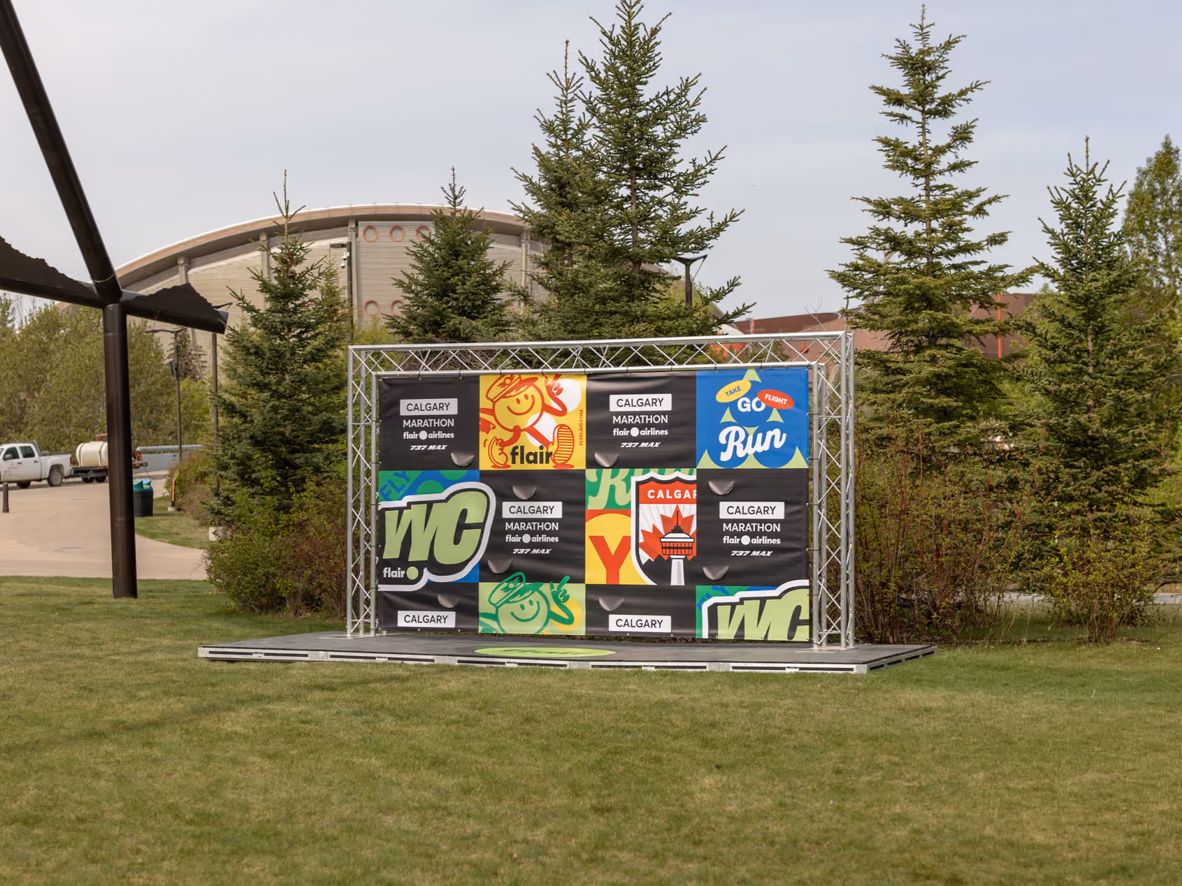 Three-quarter view of the photo backdrop on its stage at the edge of a lawn, beside a dark metal sculpture.