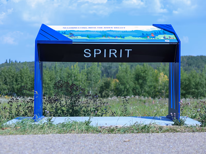 Blue steel interpretive sign reading "Spirit," surrounded by wildflowers near the solar farm pathway.
