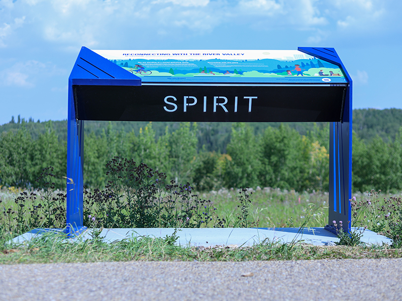 Blue steel interpretive sign reading "Spirit," surrounded by wildflowers near the solar farm pathway.
