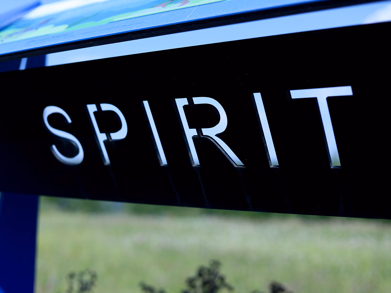 Close-up of laser-cut "Spirit" lettering on a black powder-coated steel panel.