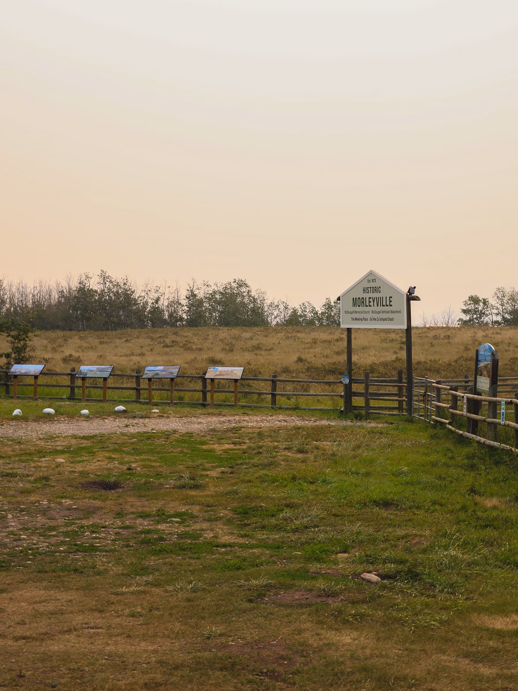 Historic Morleyville entrance sign and row of interpretive panels along the fence at dusk.