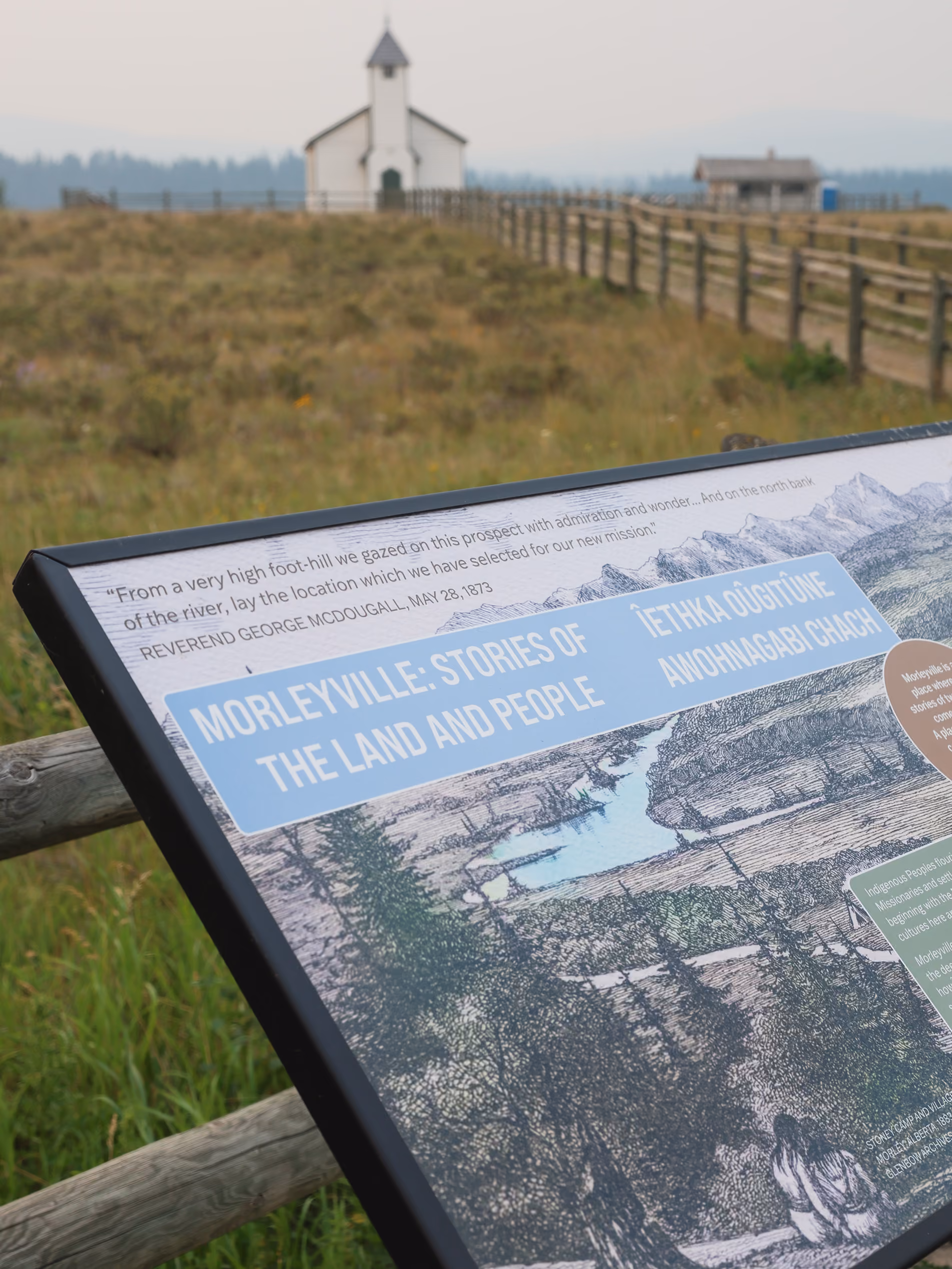 Close-up of an interpretive trail panel with the historic church visible in the softly focused background.