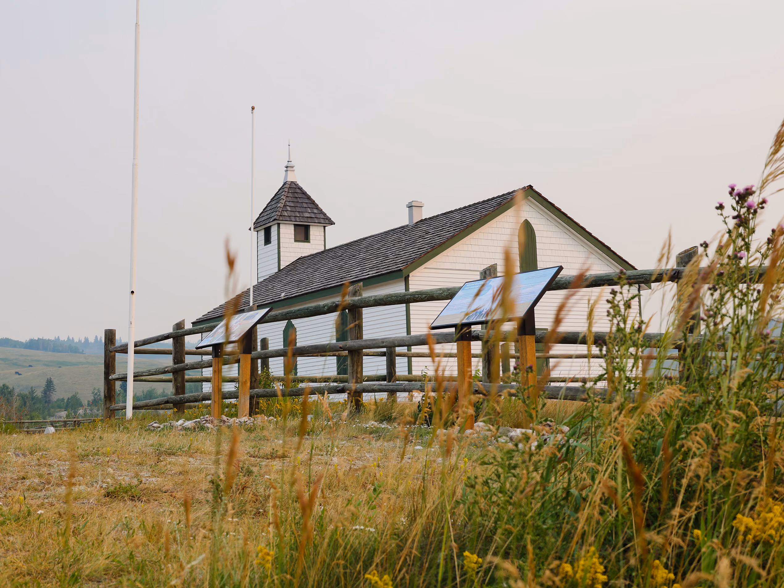 McDougall Memorial Church framed by prairie grass with two interpretive trail panels in the foreground.