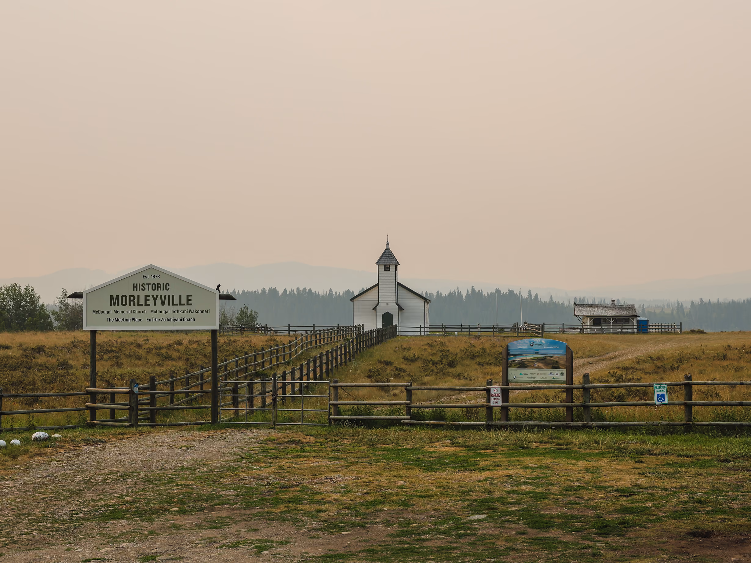 Historic Morleyville entrance sign and welcome panel with the church and grounds beyond the fence line.