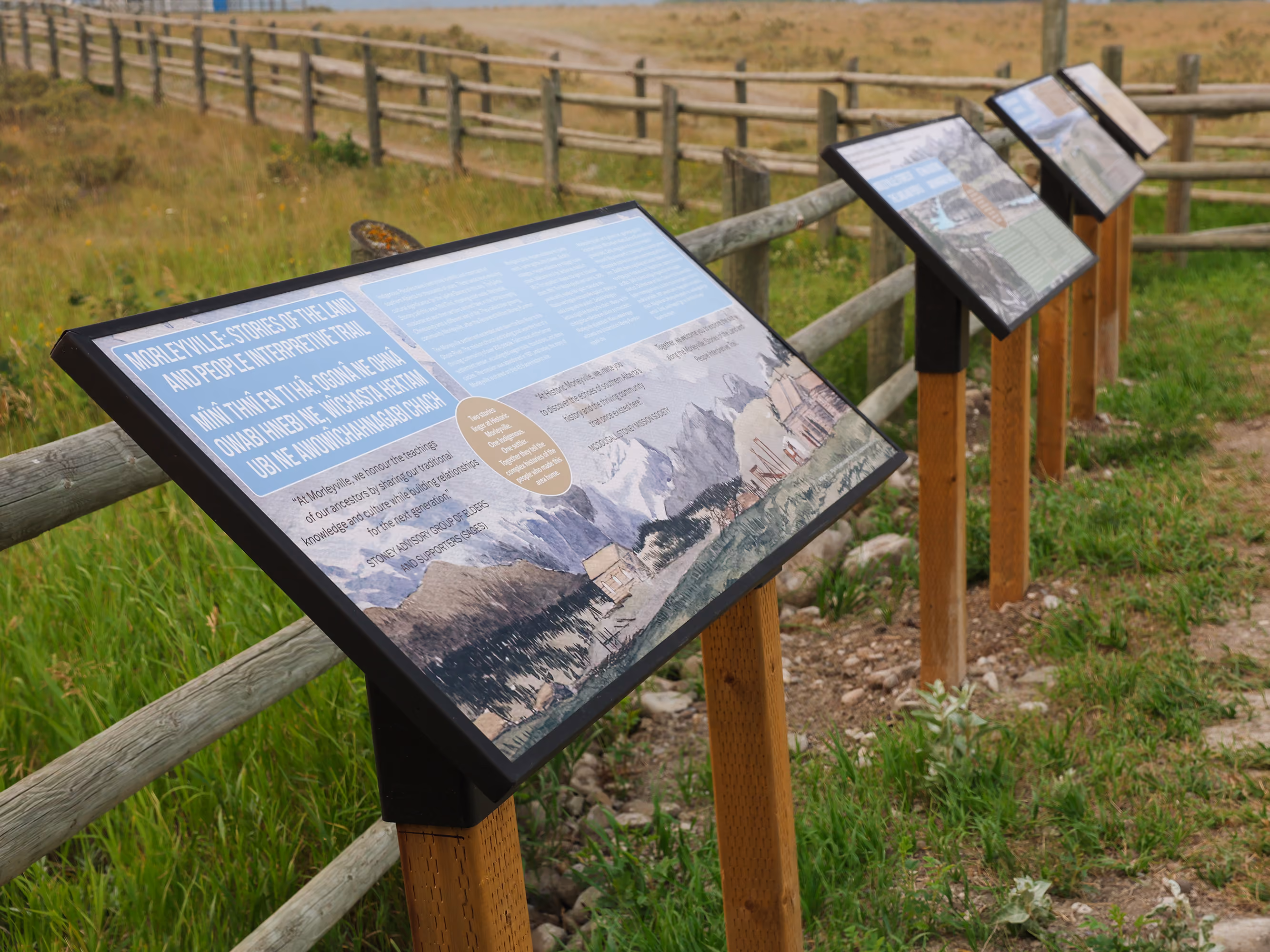 Row of angled interpretive panels along the fenced trail path leading toward the historic site.