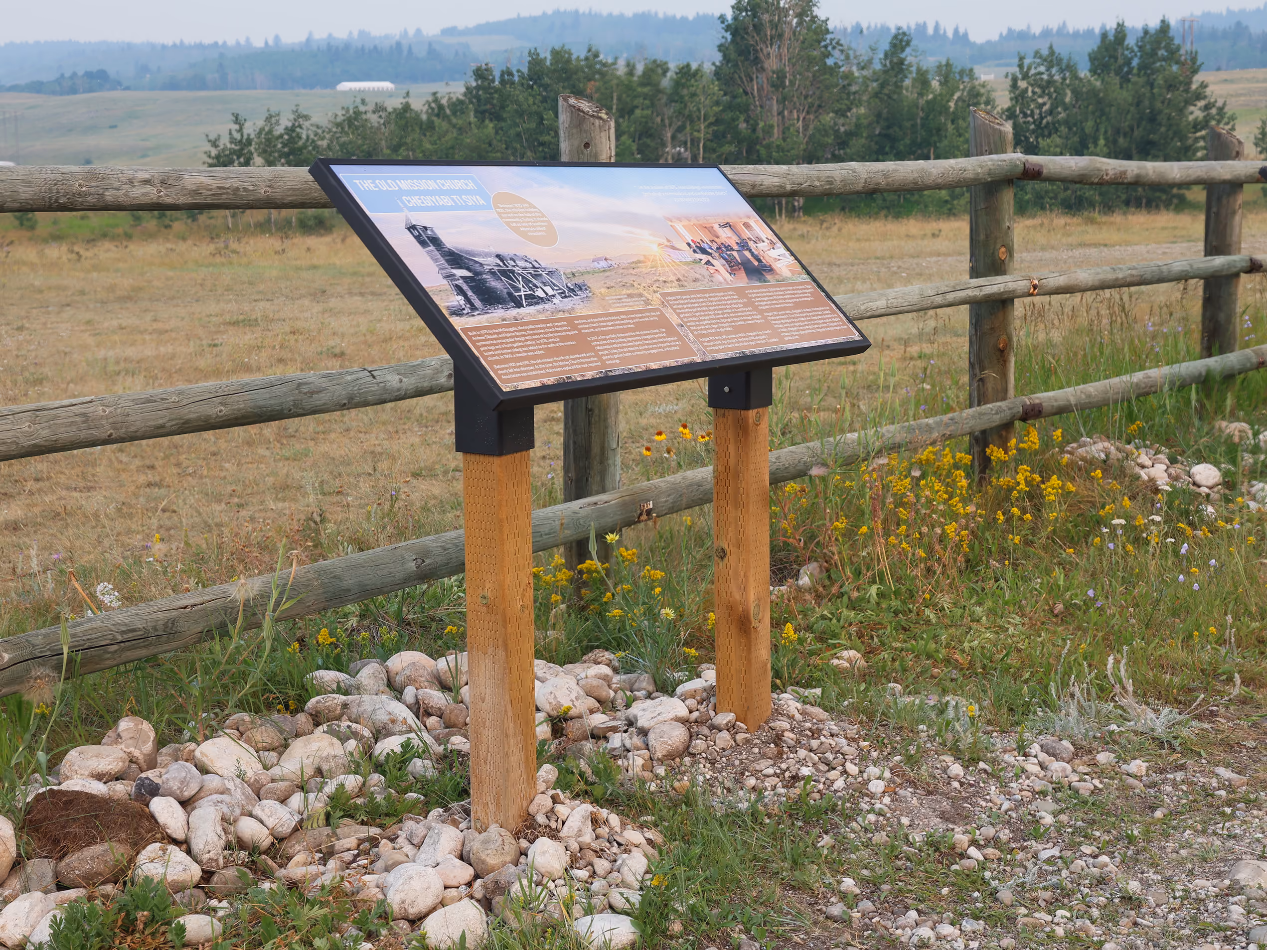 "The Old Mission Church" interpretive panel mounted along the rail fence with hills in the distance.