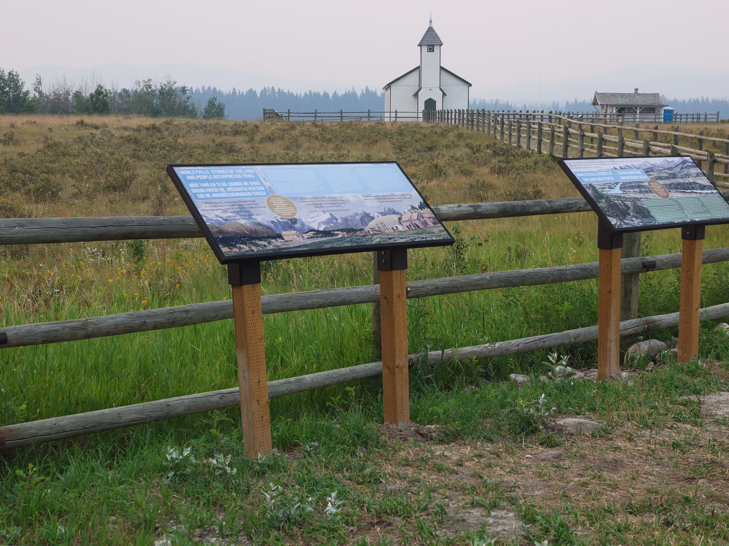 Two bilingual interpretive panels along the fence line with McDougall Memorial Church in the background.